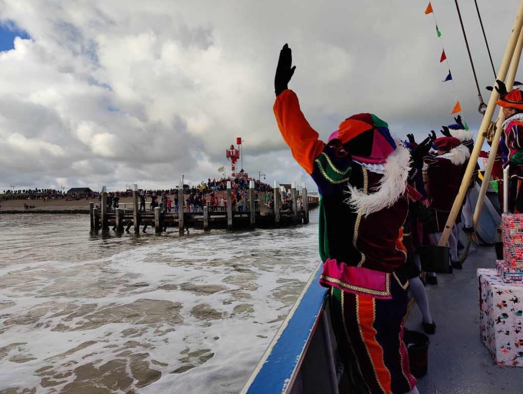 Piet zwaait vanaf de boot naar het publiek bij aankomst in de haven van Oudeschild