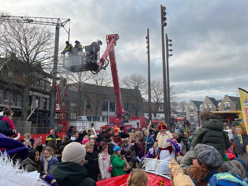 Sinterklaas in een open auto tussen het publiek, met Pieten in een hoogwerker